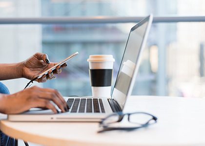 Close-up of hands typing on a laptop while holding a cell phone.